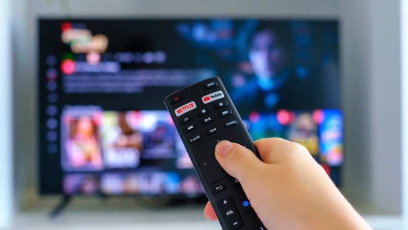 Ruka drži daljinski upravljač ispred televizora sa otvorenom Netflix aplikacijom