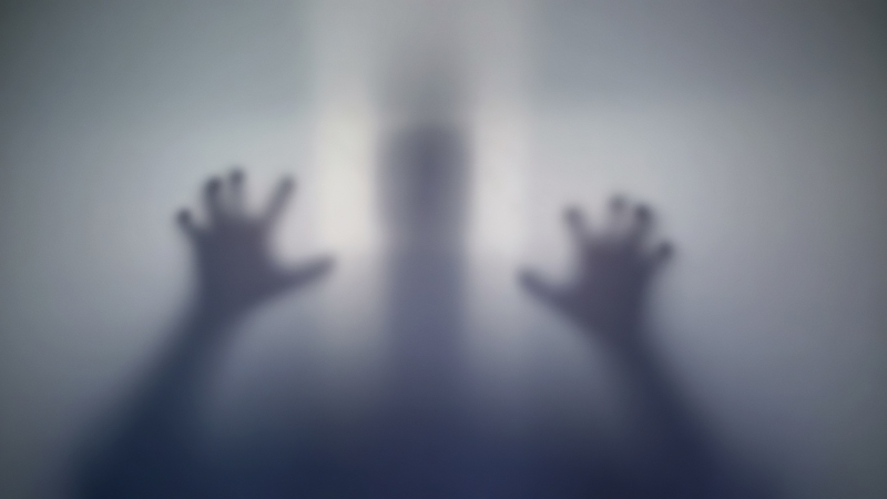 Zamagljena silueta osobe sa podignutim rukama iza stakla, kao scena iz horor filma o zombijima